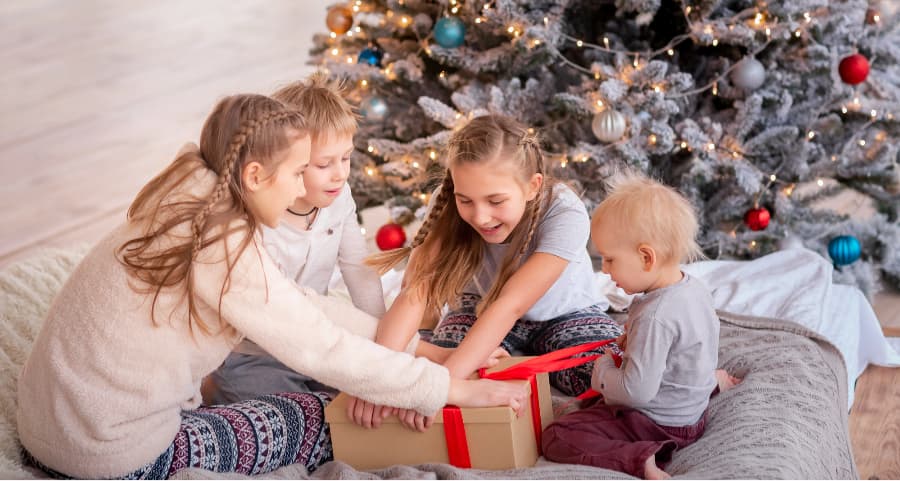 Children opening a present in the living room next to a Christmas tree.